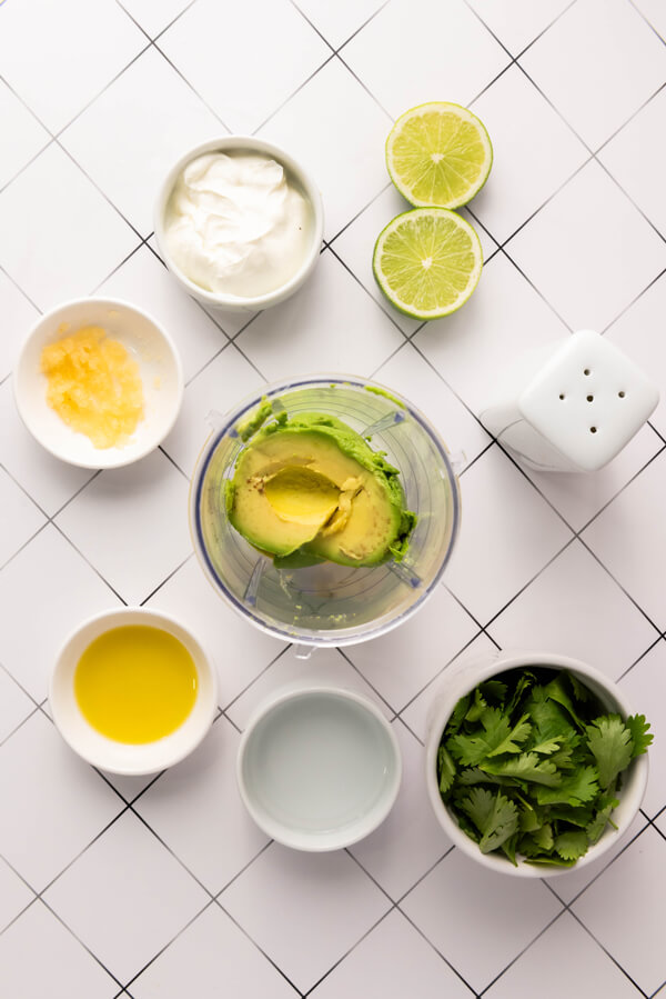 Kitchen counter top with avocados, sour cream, lime juice, garlic, fresh cilantro, olive oil, and salt