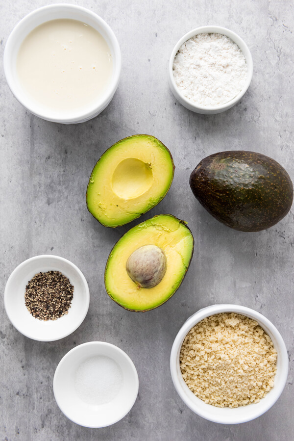 Two avocados next to bowls of panko, flour, soy milk, salt, and pepper