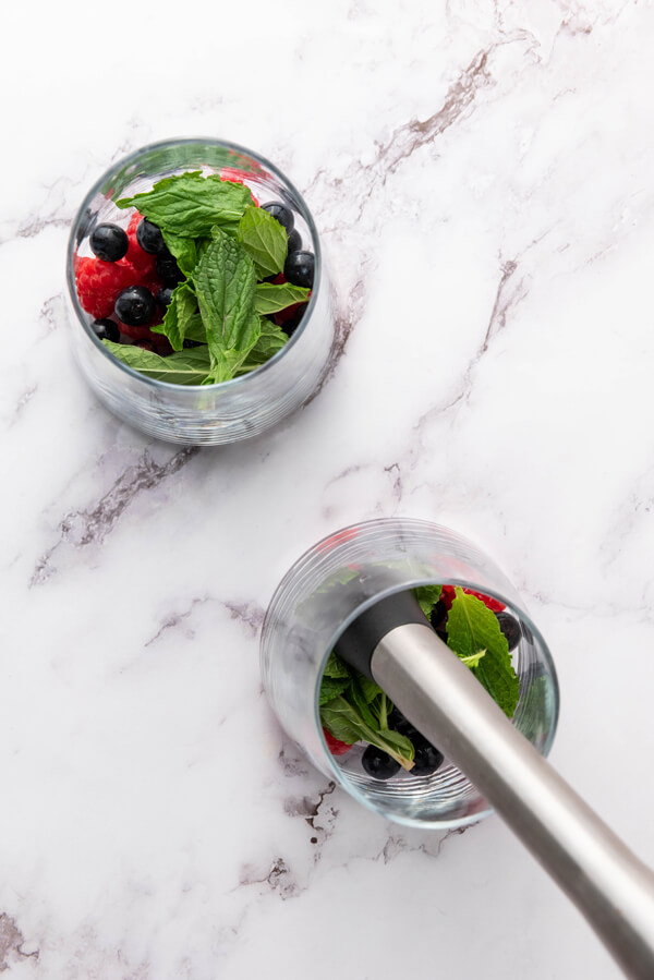 Mashing blueberries, raspberries, and mint leaves