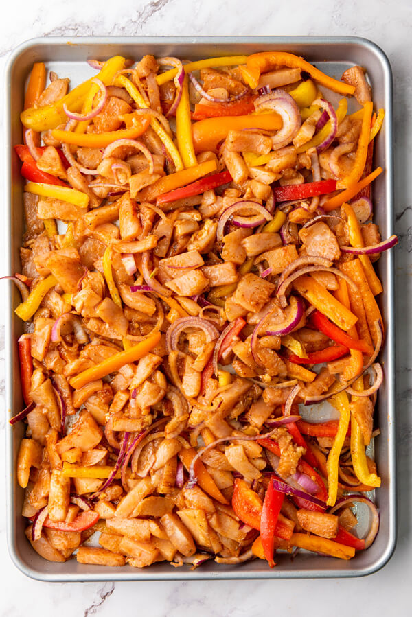 Spreading the chicken and veggie mixture evenly across a sheet pan 