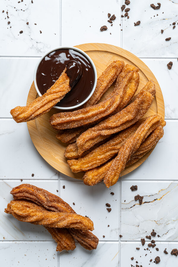 Churros on a plate next to a cup of chocolate sauce