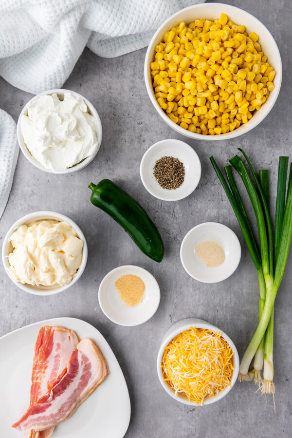 Counter top with scallions, jalapeno, and bowls with corn, mayonnaise, sour cream, shredded cheese, bacon, pepper, garlic powder, and onion powder