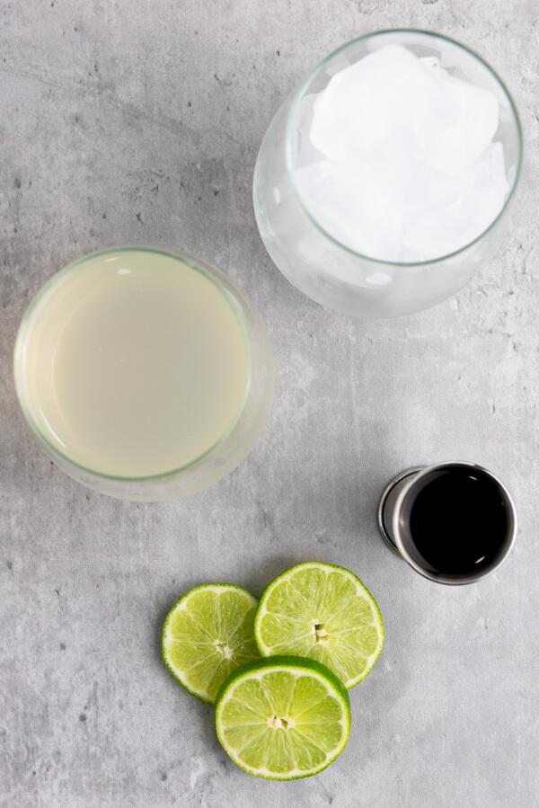 Counter top with limes and three glasses filled with dark rum, ginger beer, and ice cubes