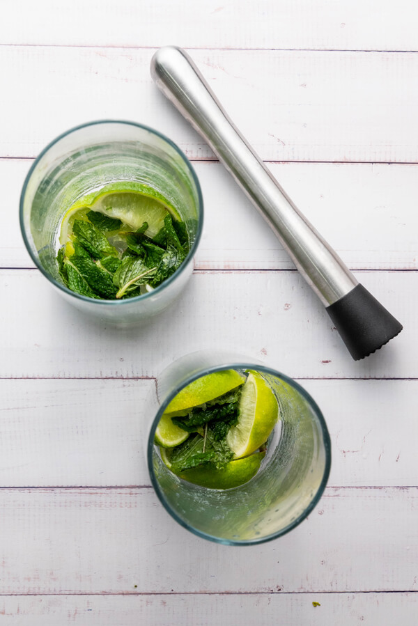 Muddling lime wedges, fresh mint leaves, and sugar