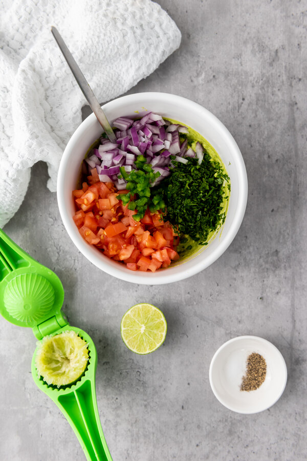 Mixing the avocado, tomatoes, onions, jalapeños, cilantro, lime, salt, and pepper