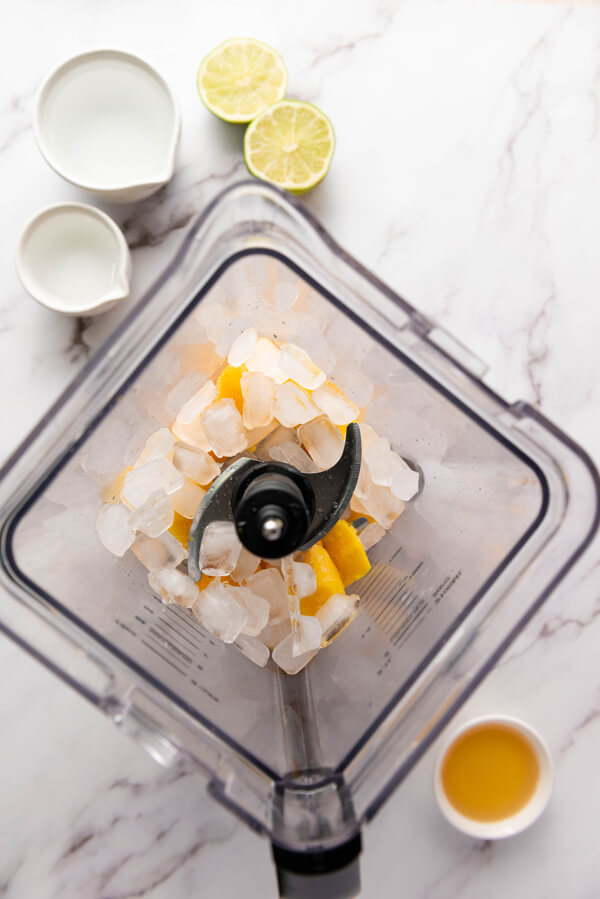 Combining frozen mango chunks, ice cubes, tequila, triple sec, lime juice, and agave syrup in a blender