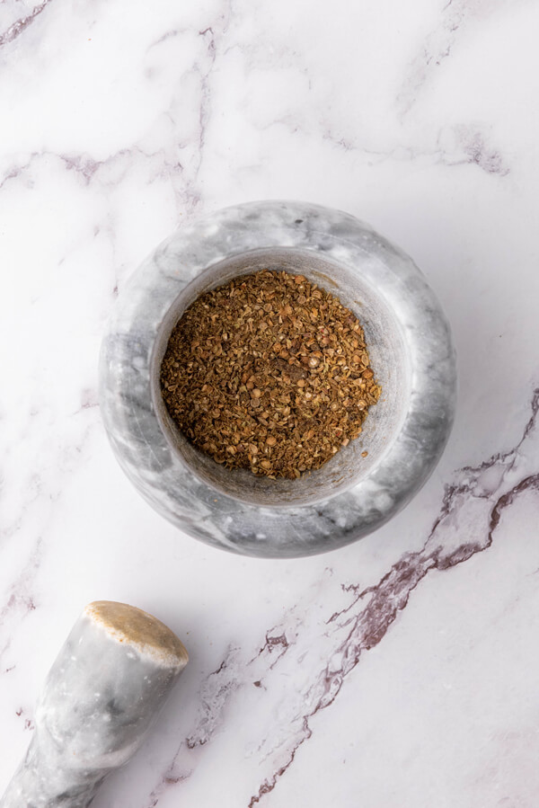 Grinding cumin, coriander, peppercorns, cloves, and oregano 