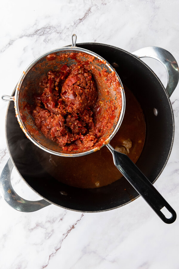 Straining the blended sauce and stirring it back into the pot 