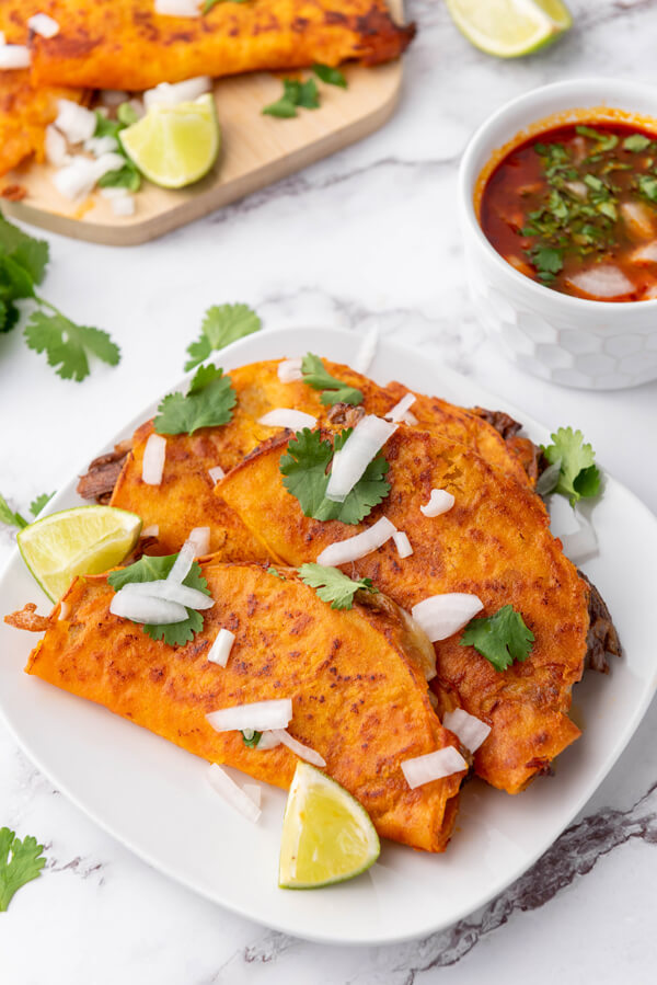 Serving the quesabirria tacos with cilantro leaves, lime wedges, diced onions. and the consomé
