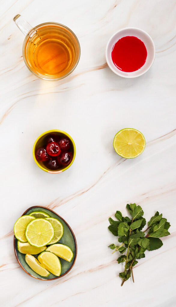 Kitchen counter top with ginger ale, grenadine syrup, Maraschino cherries, limes, and mint leaves