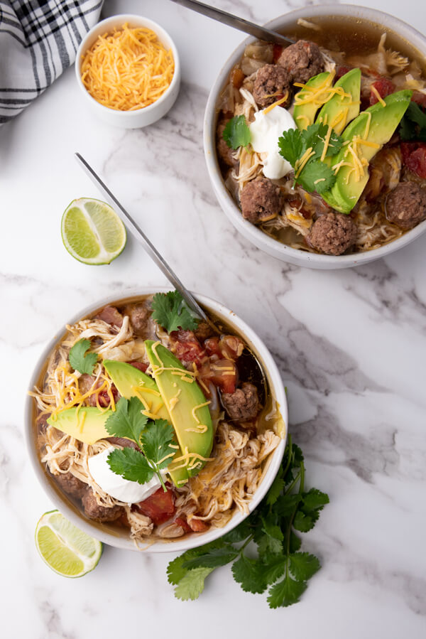 Serving the taco soup with Mexican shredded cheese, slices of avocado, a squeeze of lime, cilantro, and sour cream