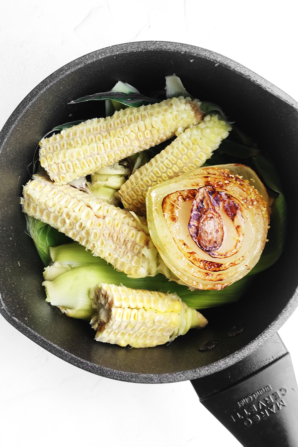 Adding corn cobs and husks, onion, garlic, bay leaves, and peppercorns to a pot