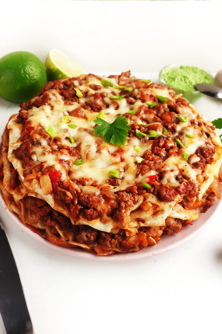 Serving Mexican Lasagna with cilantro on top and lime wedges and guacamole on the side