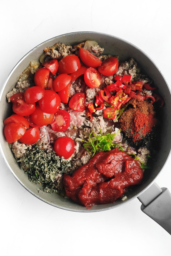 Adding tomatoes, chopped chili, lime zest, spices, and tomato sauce