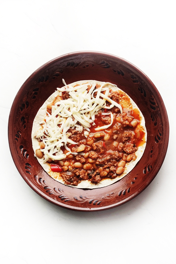  Adding a layer of the beef mixture over a tortilla, followed by cheese