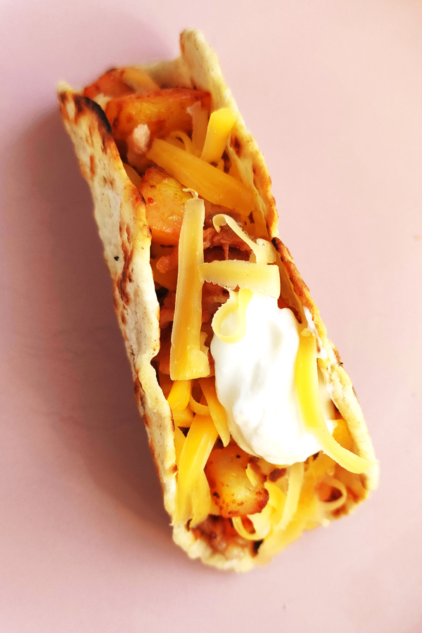 Serving potato taco with sour cream and grated cheese