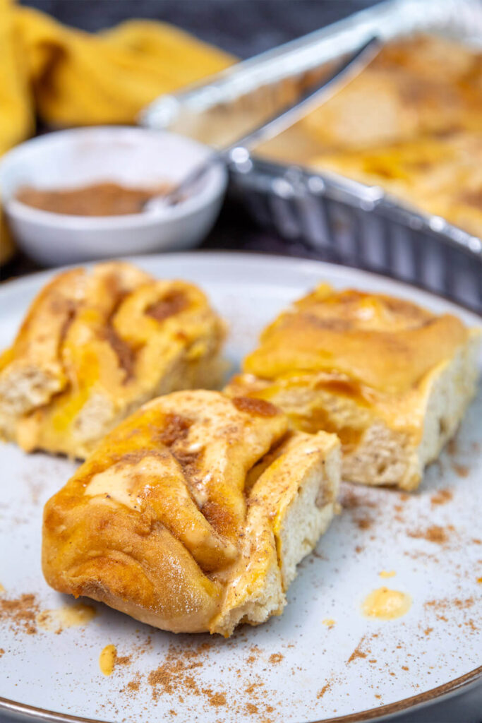 Serving the pumpkin cinnamon rolls with frosting and extra cinnamon