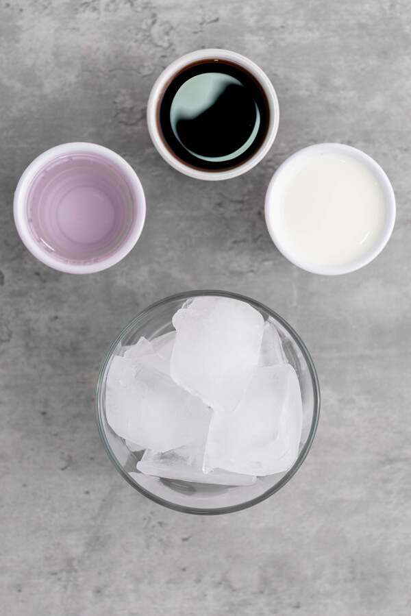 Glass filled with ice cubes next to cups of vodka, coffee liqueur, and heavy cream