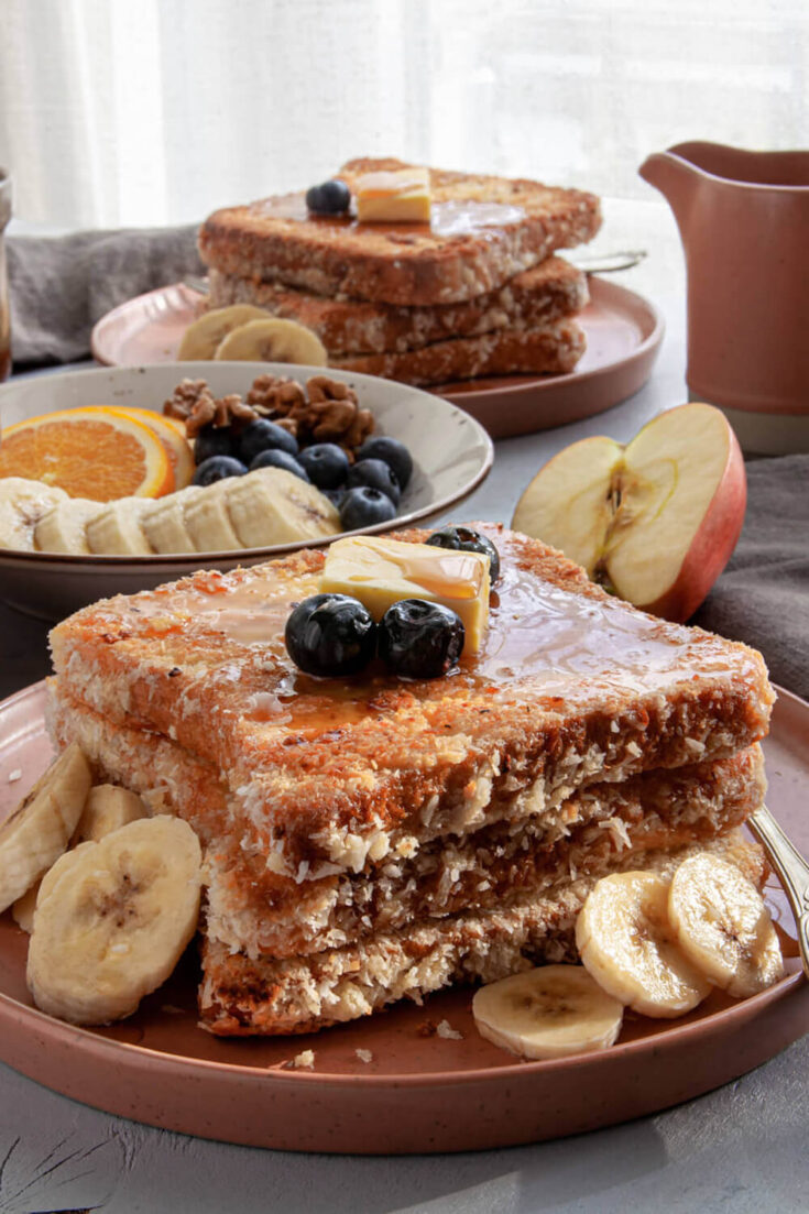 Serving the coconut french toast with butter, maple syrup, banana slices, orange slices, and fresh berries