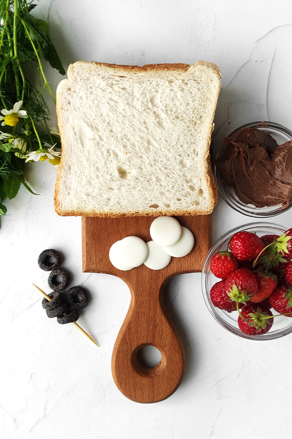 White table with white bread, Nutella, berries, chamomile, mint, white chocolate chips, and ring shaped cereal