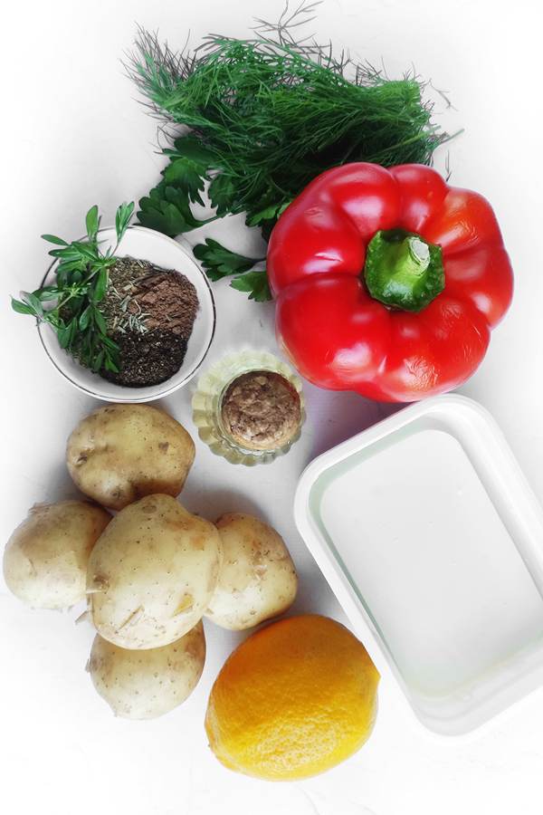 White table with potatoes, a bell pepper, a lemon, olive oil,  feta cheese, dill, and parsley