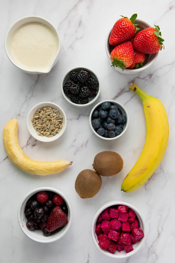 Marble table with bananas, kiwis, blueberries, blackberries, strawberries, raspberries, cherries, dragon fruits, and a cup of oatmeal