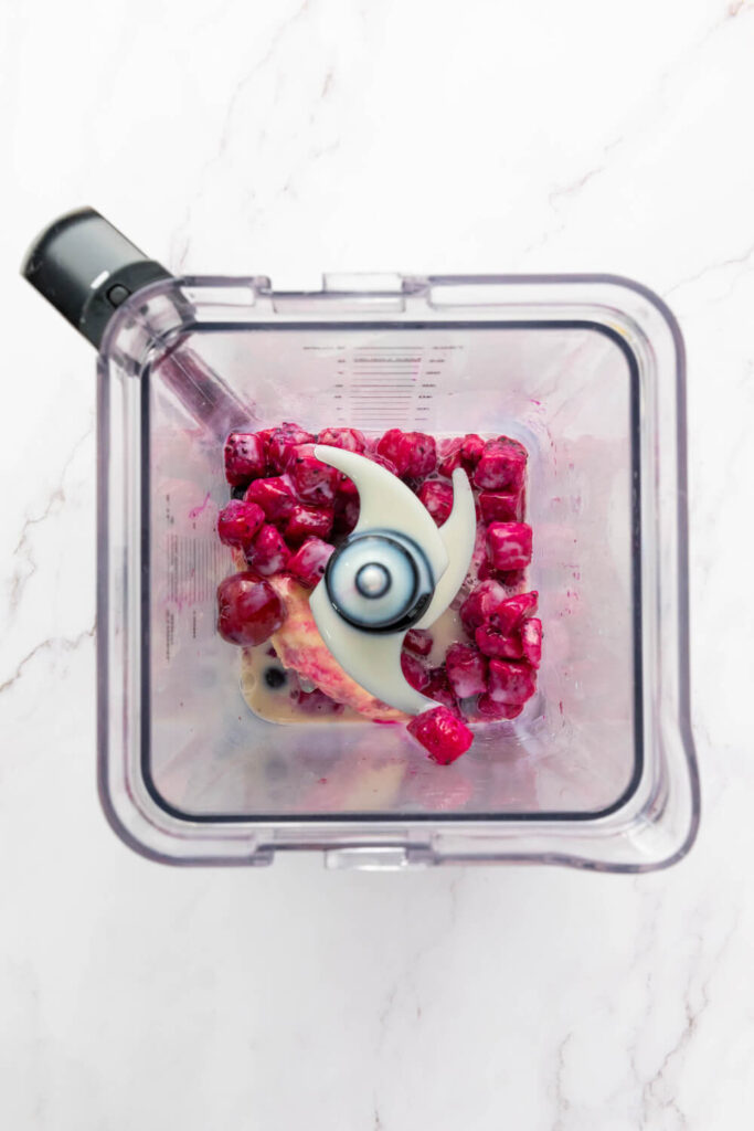 Adding frozen banana, dragon fruit cubes, mixed berries, and milk to a blender