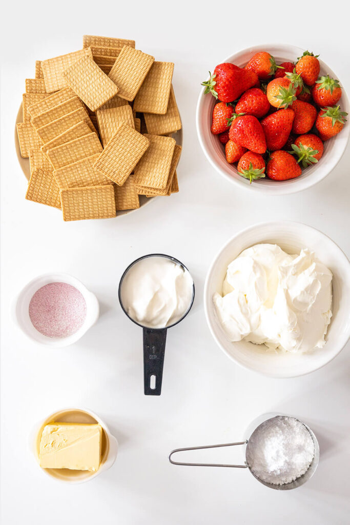 White table with cups of strawberries, cookies, gelatin, butter, powdered sugar, cream cheese, and whipped cream