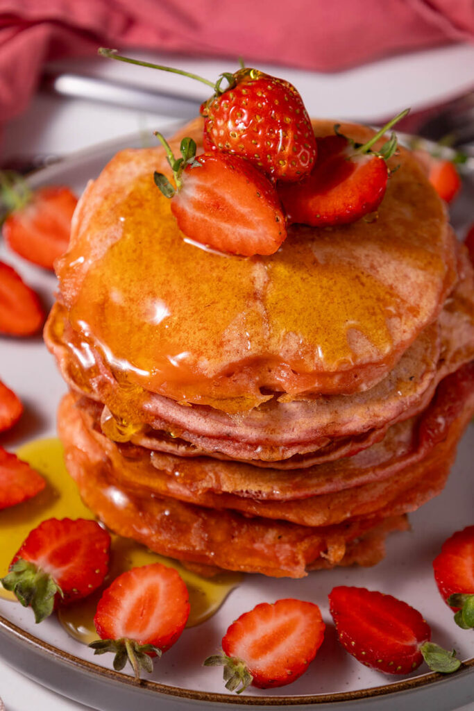 Serving strawberry pancakes with maple syrup and extra berries
