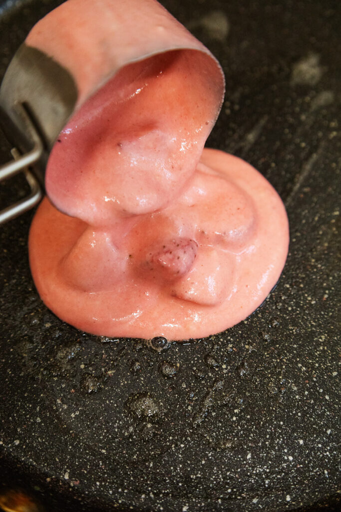 Adding 1/3 cup of batter onto a hot skillet