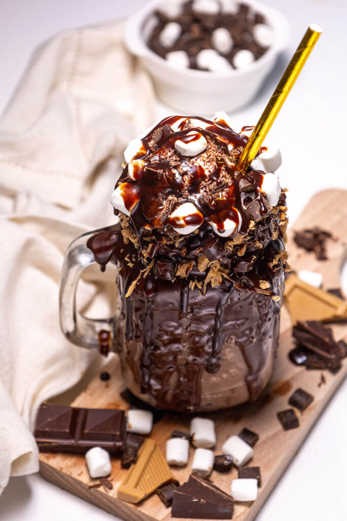 Serving the chocolate freakshake with whipped cream, marshmallows, chocolate chips, and chocolate sauce