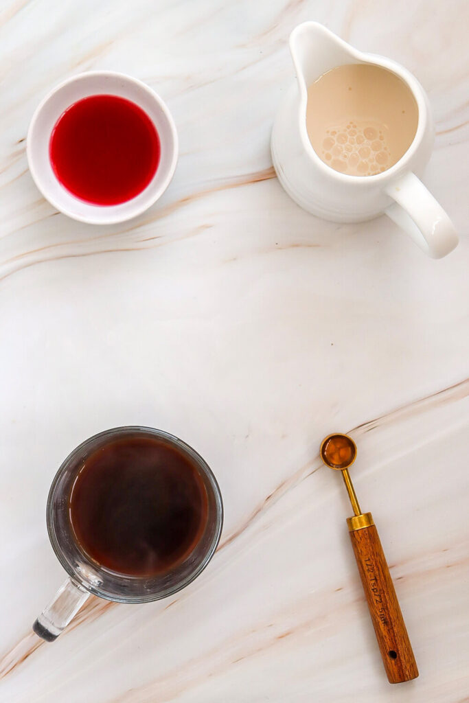 Marble table with bowls of coffee, lavender syrup, milk, and a spoon of vanilla extract