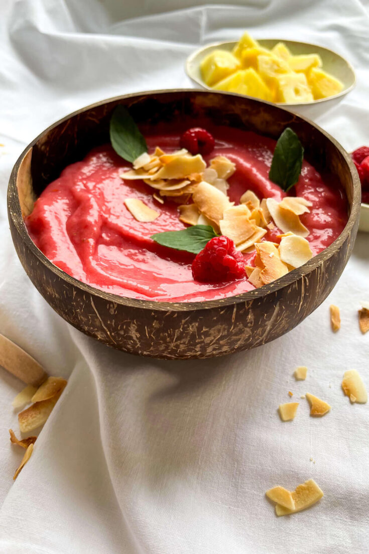 Serving the raspberry pineapple smoothie bowl with Greek yogurt, coconut flakes, and extra raspberries