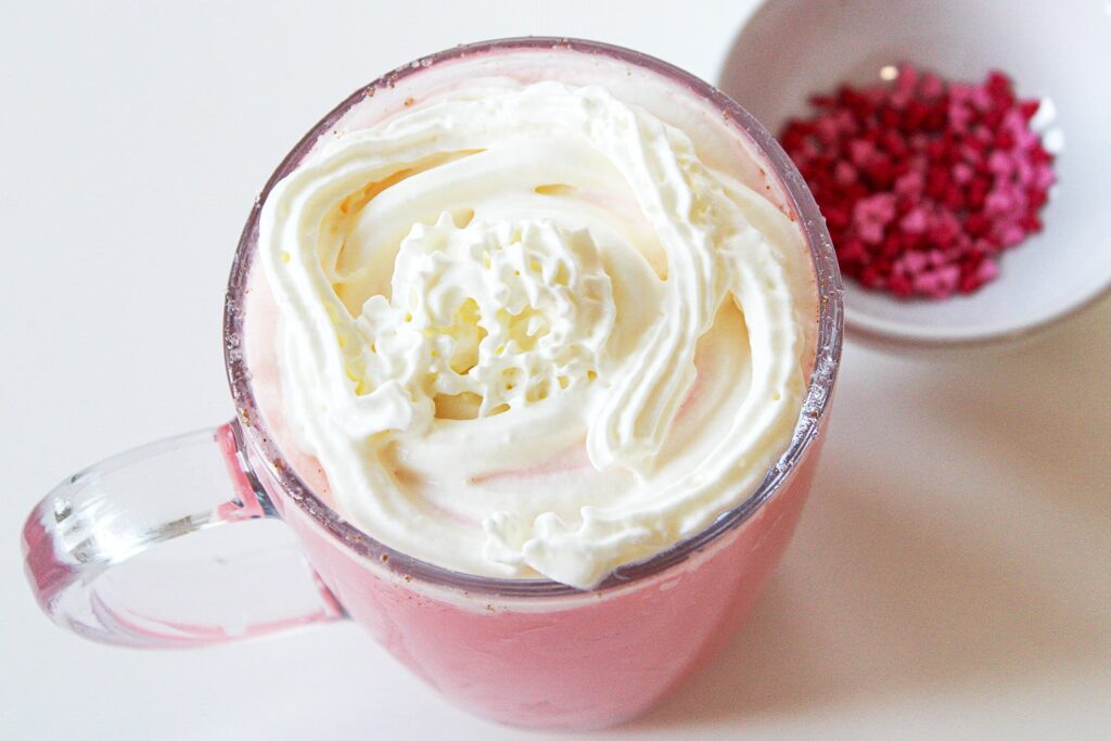 Pouring the chocolate mix into a mug and adding a swirl of whipped cream