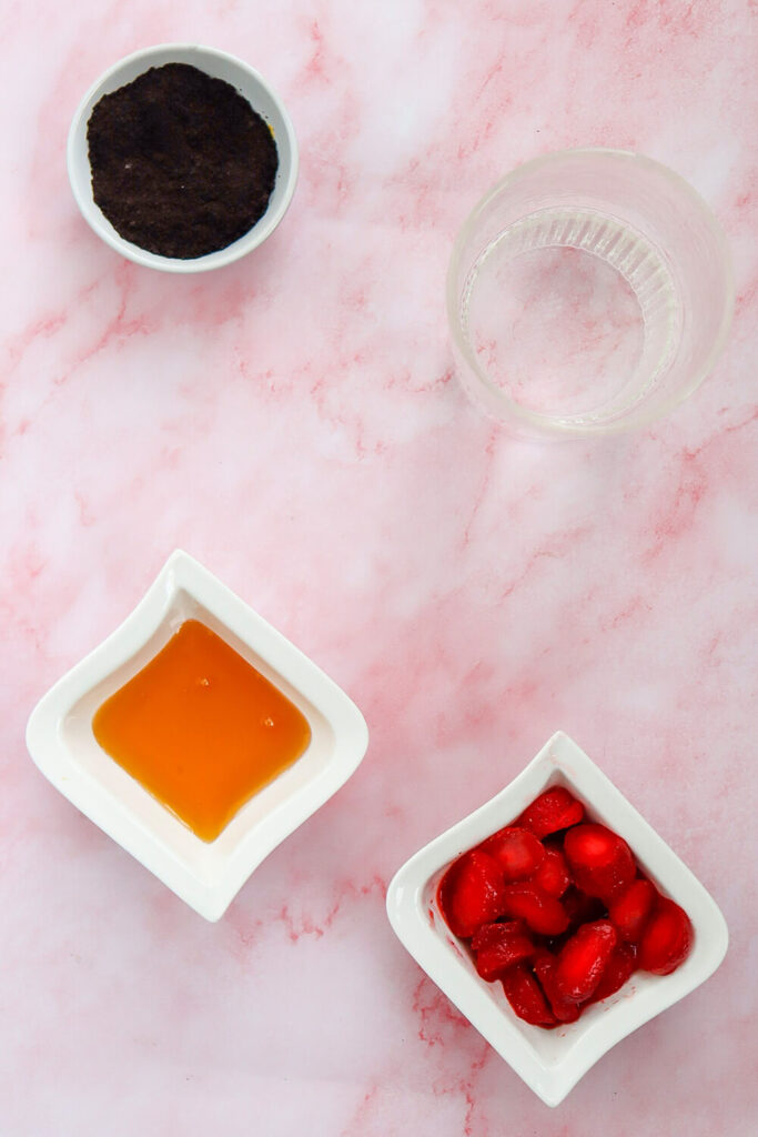 Pink marble countertop with bowls of acai powder, coconut water, honey, and frozen strawberries